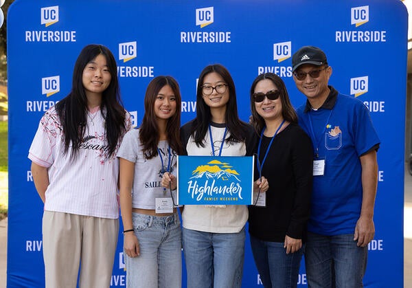 A family of 5 people posig for a photo in front of a step-and-repeat banner with the UC Riverside Logo.