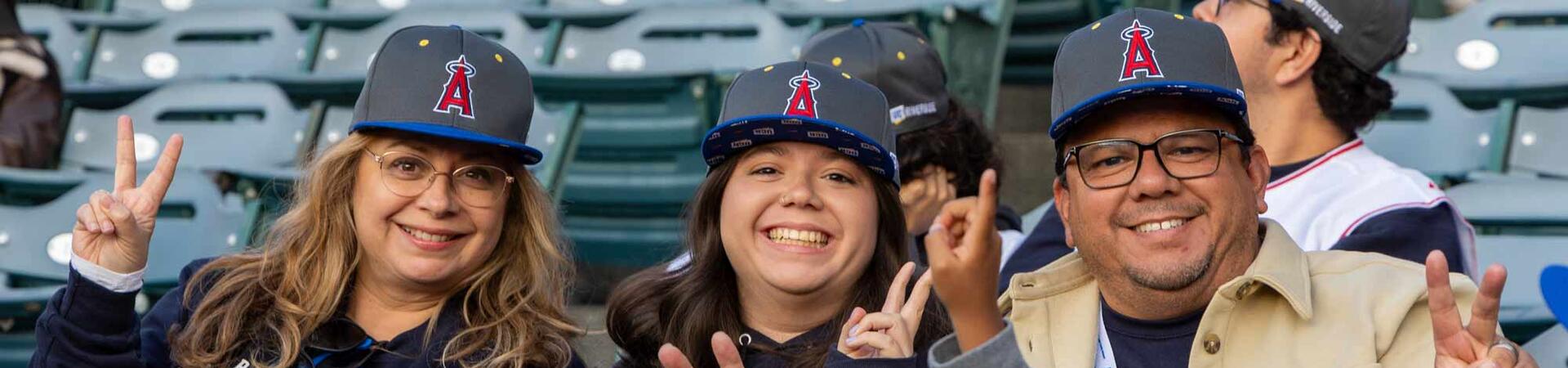 3 baseball fans are holding up peace signs with their fingers.